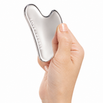 A hand holding a silver metallic gua sha massage tool with the brand name 'LOVE & PEBBLE' printed on it, set against a solid white background.