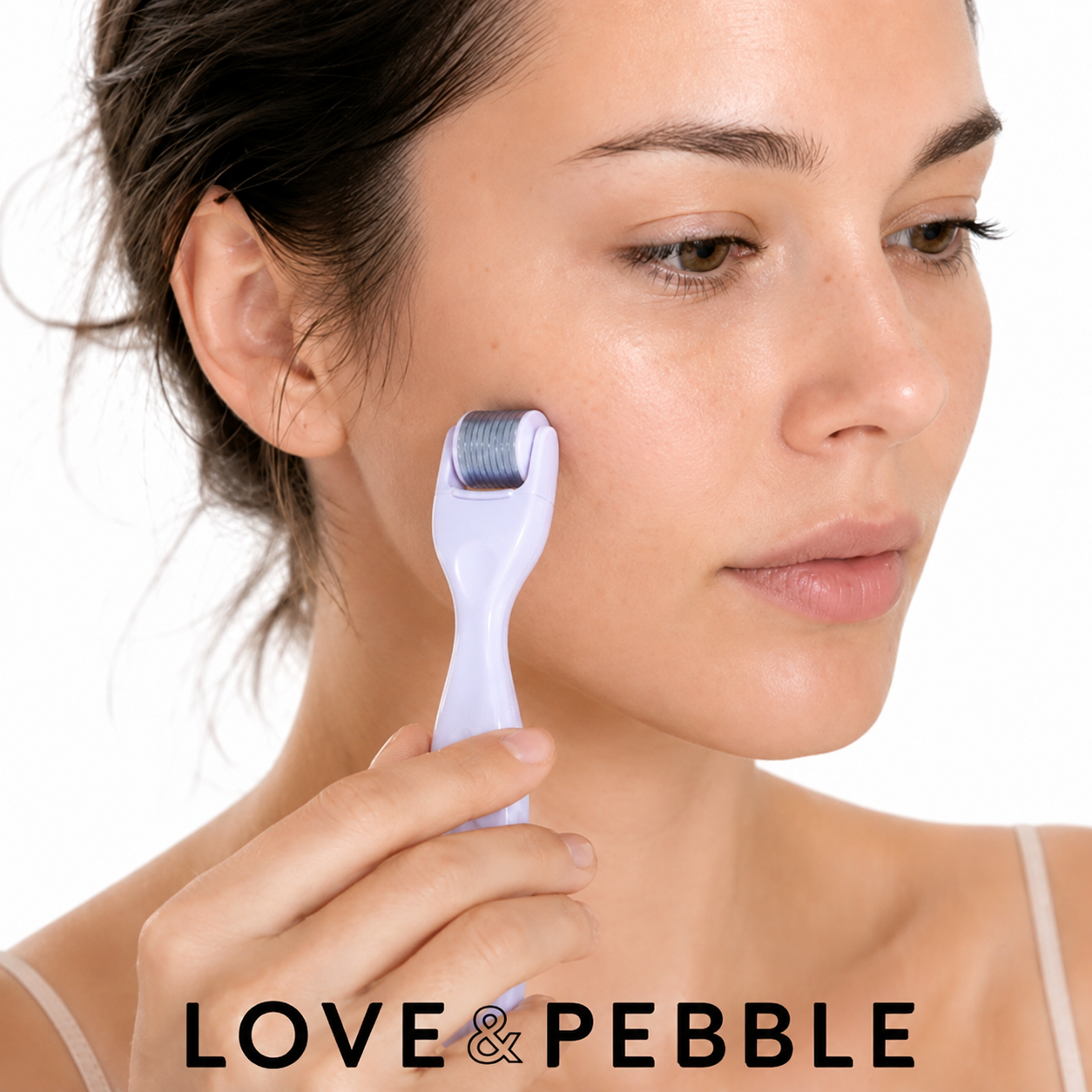 A woman holding a light purple dermal roller tool against her cheek, with the brand name LOVE & PEBBLE displayed at the bottom.